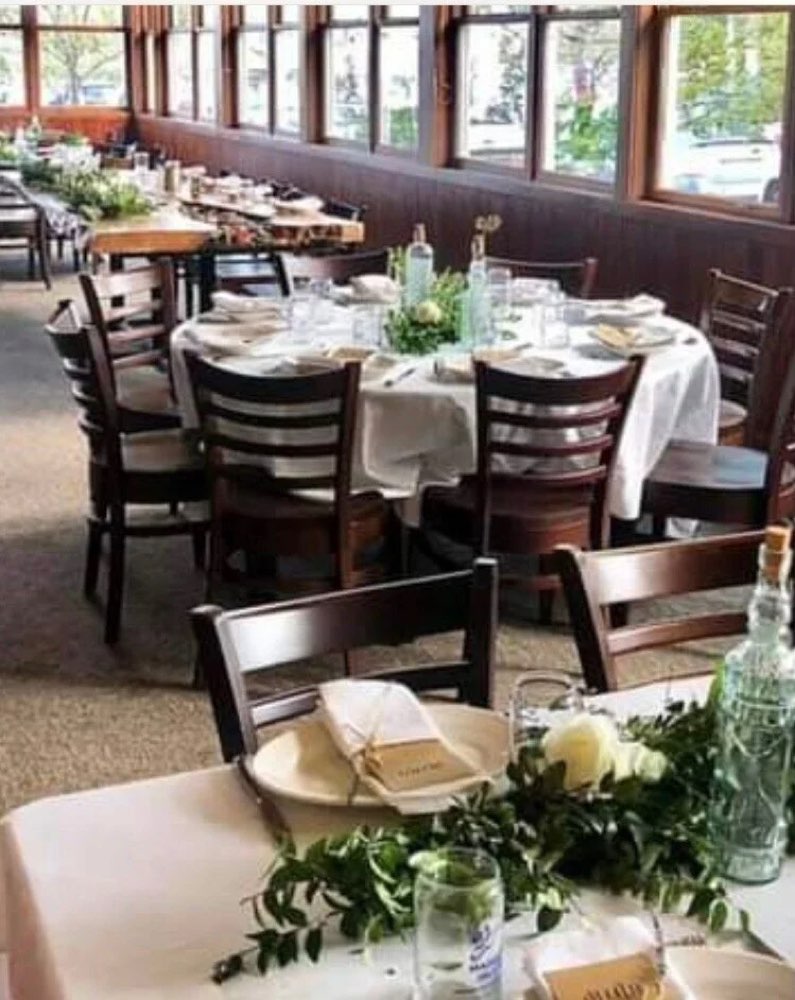 A long table set with linens, glasses and greenery by the windows